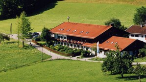 Ein Landhotel mit rotem Ziegeldach, umgeben von üppigen grünen Feldern und bewaldeten Hügeln.