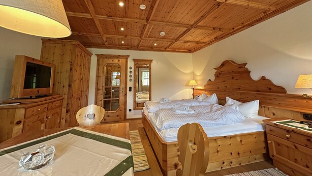 Ein Zimmer mit Holzboden, einem Bett, einem Fernseher und einer Tür zu einem anderen Raum.
