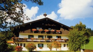 Ein mehrgeschossiges Gebäude mit Balkonen, die mit Blumen geschmückt sind, umgeben von einem gepflegten Rasen und Bäumen.