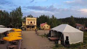A rustic hotel with a yellow facade, outdoor seating with yellow umbrellas, and a tent set up nearby.