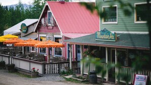 A rustic building with a green exterior and a red roof, featuring outdoor seating with orange umbrellas. - McCarthy Lodge Resort (McCarthy)