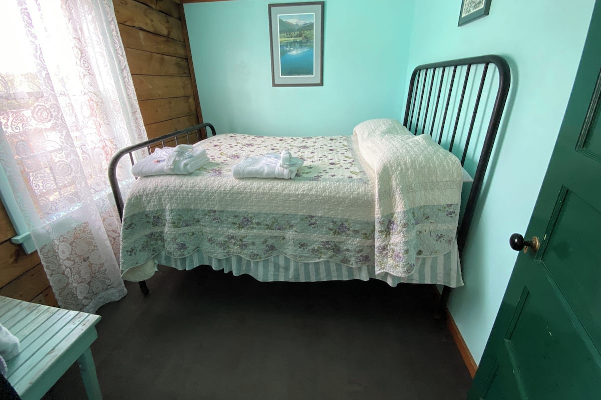A single bed with a floral bedspread, a wooden headboard, a framed picture on the wall, and a green door.