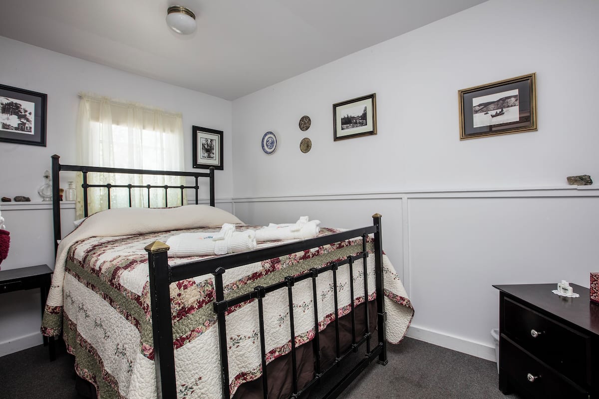 A bedroom with a bed, a nightstand, a dresser, and a window with curtains.