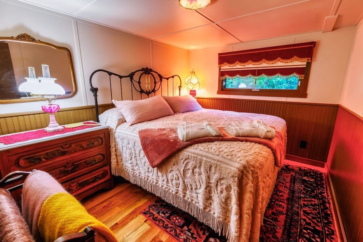 A bedroom with a large bed, a dresser, a mirror, and a window with curtains.
