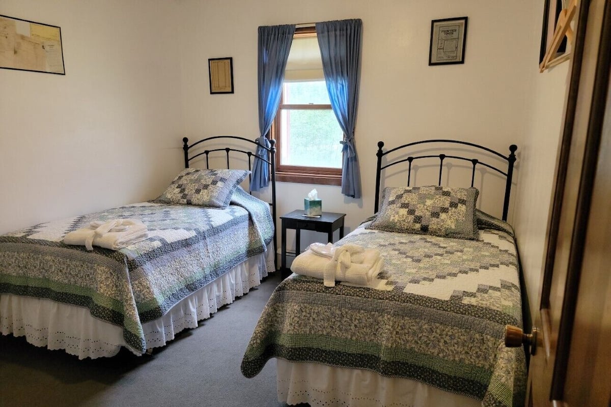 A bedroom with two single beds, a small table, and a window with curtains.