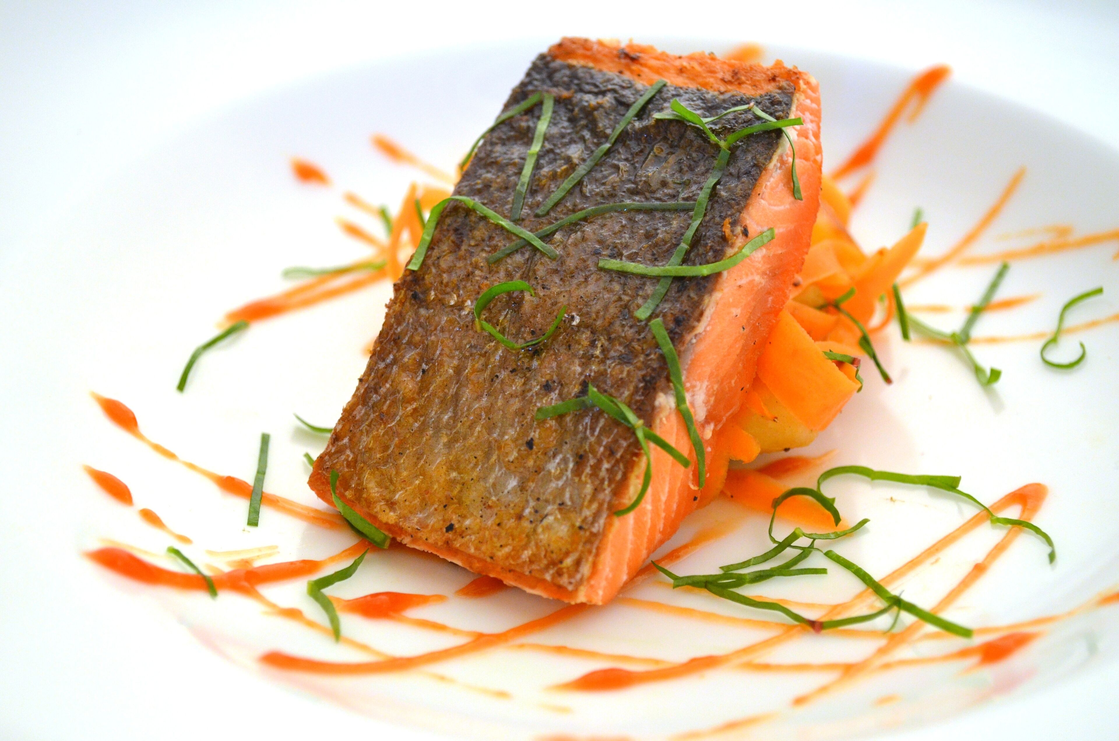 A piece of salmon on a white plate with carrot garnish.