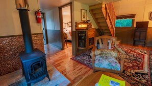 A cozy living room with a wood-burning stove, a staircase, and a floral armchair. - McCarthy Lodge Resort (McCarthy)