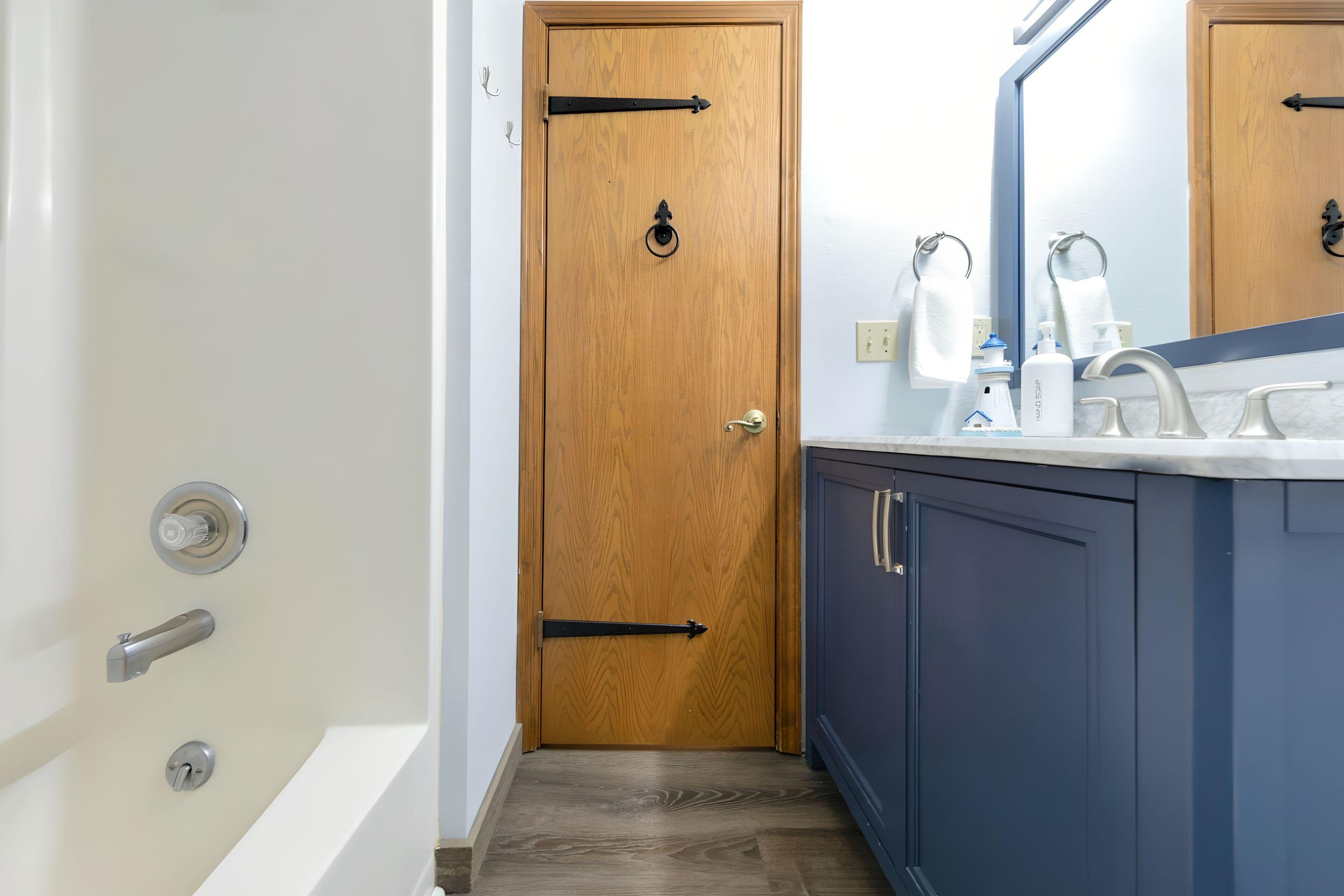 Ein Badezimmer mit Holztür, einer weißen Badewanne, einem blauen Waschtisch mit Spiegel und einem weißen Handtuch an der Wand.