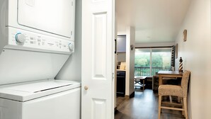 A laundry area with a white washing machine and dryer, a wooden dining table with chairs, and a view of the outdoors through a large window. - Aurora at Nautilus (Ocean Shores)