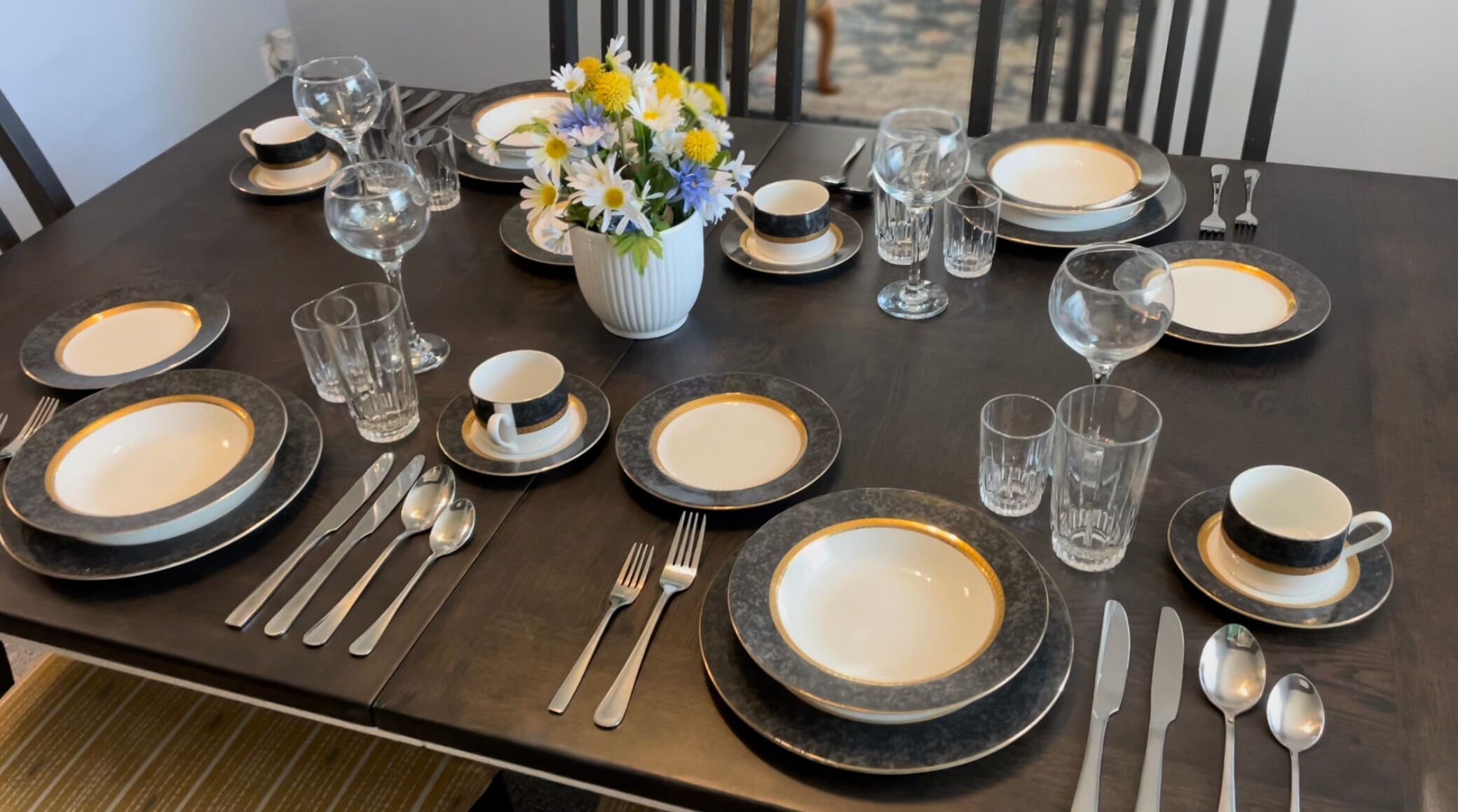 A dining table set with plates, cutlery, glasses, and a vase with flowers.