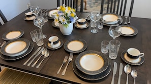 A dining table set with plates, cutlery, glasses, and a vase with flowers.