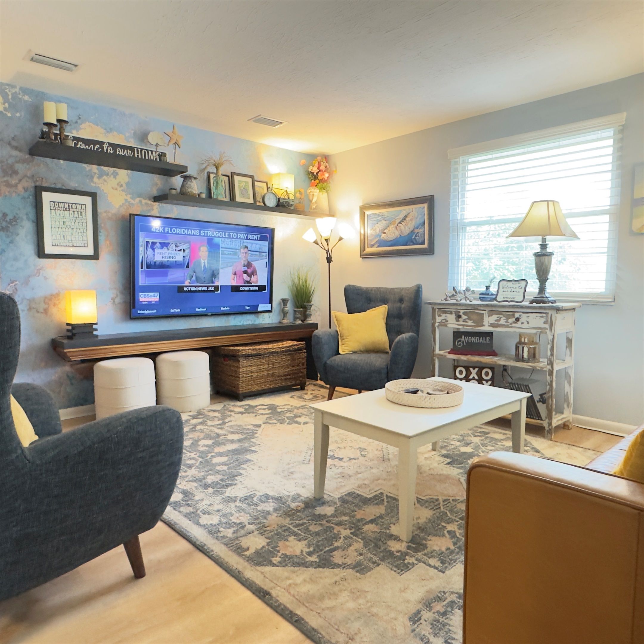 A living room with a flat-screen TV, a coffee table, a blue armchair, and a bookshelf.
