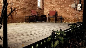 Una terraza de madera con sillas, un muro de ladrillo y una ventana.