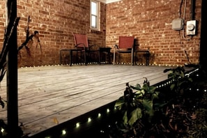 A wooden deck with chairs, a brick wall, and a window.