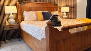 Een houten bed met hoofdeinde, een nachtkastje met een lamp en een wand met verticale latten.
