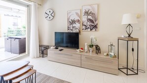 Ein modernes Wohnzimmer mit Fernseher, Sofa, Esstisch und Bildern an der Wand.