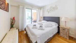 Ein Schlafzimmer mit einem Bett, einem Nachttisch, einer Lampe, einem Fenster mit Vorhängen, einem Sessel und einer Wanddekoration.