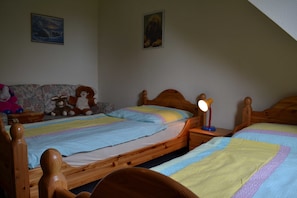 A bedroom with two wooden beds, a nightstand with a lamp, and a couch with stuffed animals. - FeWo Südwind - Reek, Renate & Reinhold (Insel Poel)