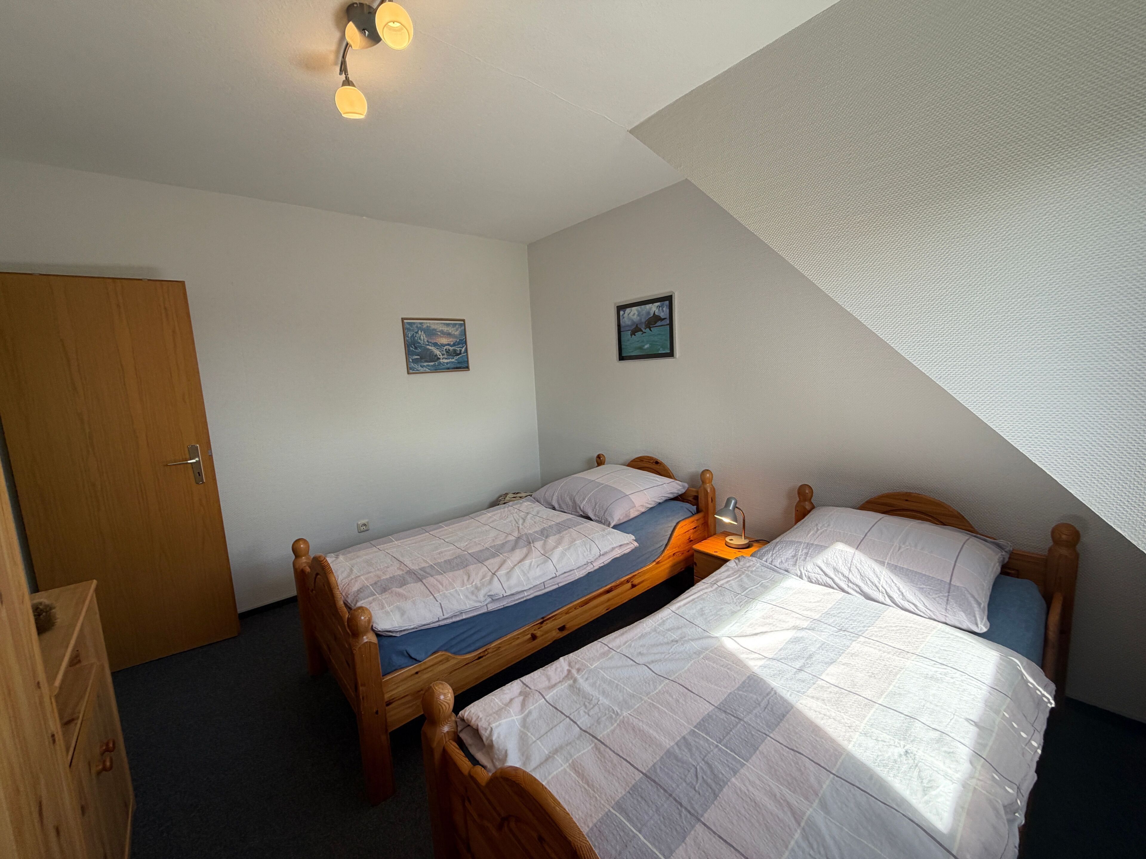 Une pièce avec deux lits en bois, une porte et un luminaire fixé au plafond.