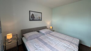 Un lit bien fait, recouvert d’une couvre-lit à carreaux, avec deux lampes de chevet, un tableau accroché au mur et un luminaire au plafond.