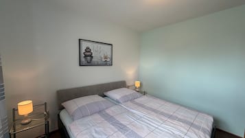 Un llit ben fet amb mantell a quadres, dues làmpades de nit, un quadre penjat a la paret i una llum al sostre.