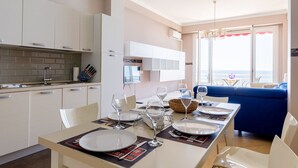 A modern kitchen with white cabinets, a dining area set for four with a view of the sea, and a blue sofa in the living area. - Wonderful Apartment on Sea (Nice)