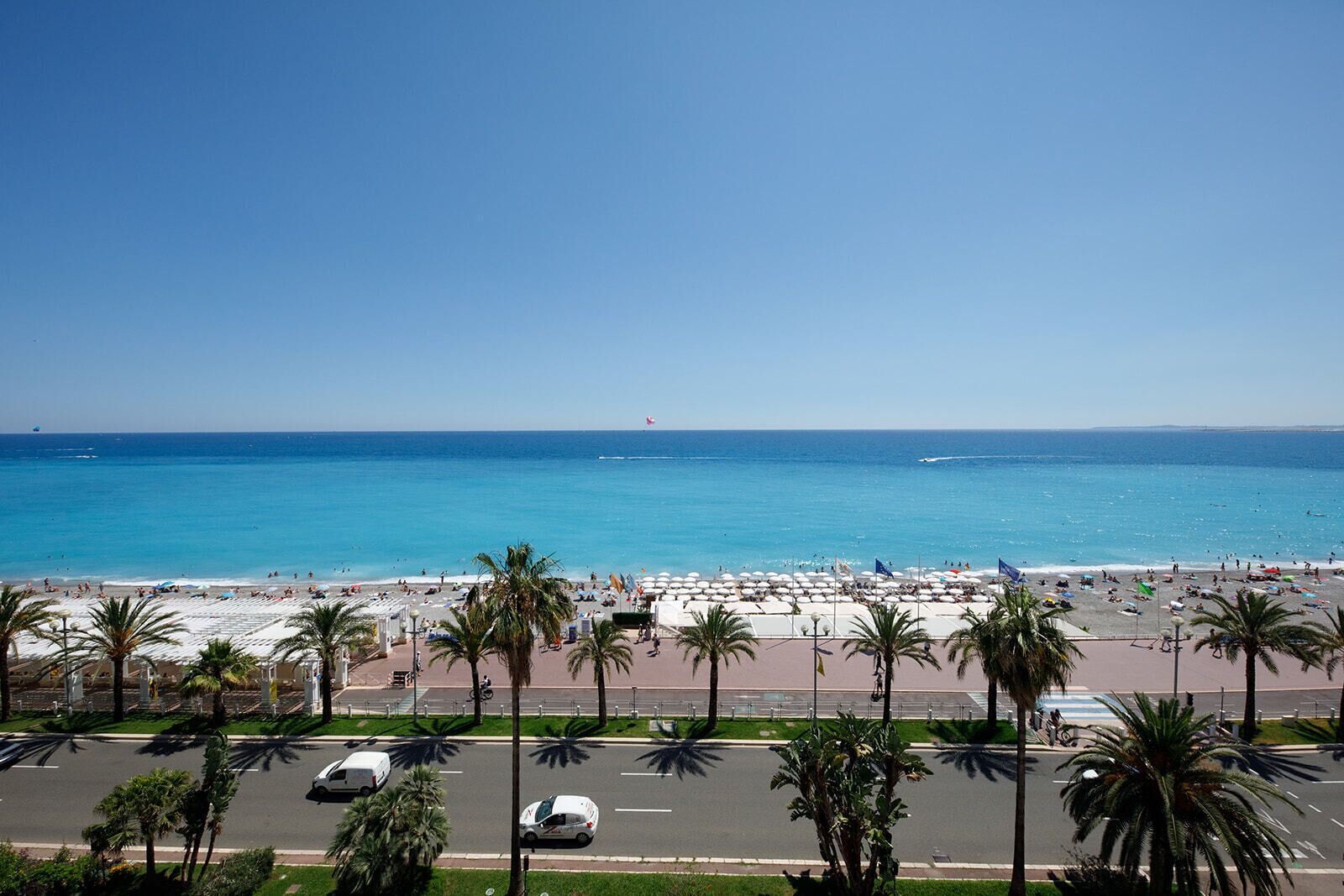 A beach with palm trees, a parking lot, and a clear blue sky.