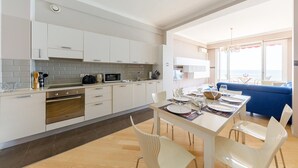 A modern kitchen with white cabinets, a dining area with a table set for four, and a blue sofa in the adjacent living area. - Wonderful Apartment on Sea (Nice)
