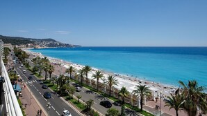 A coastal cityscape with a beach, palm-lined promenade, and clear blue sea. - Wonderful Apartment on Sea (Nice)
