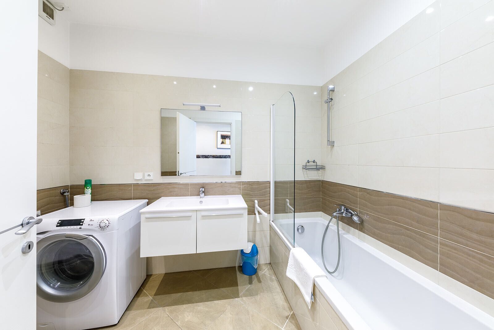 Ein modernes Badezimmer mit Waschmaschine, Waschbecken, Spiegel und Badewanne.
