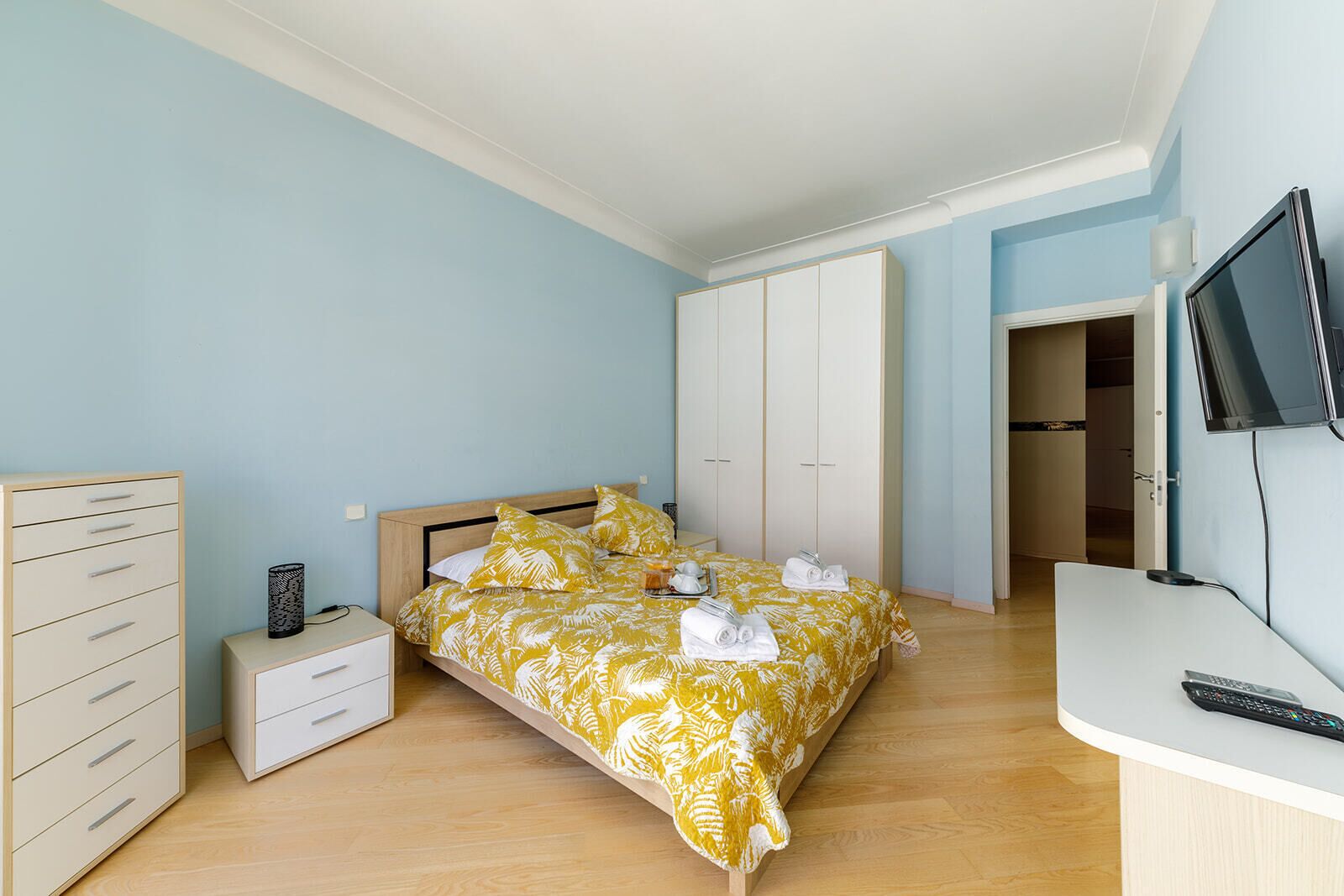 A bedroom with a bed, a nightstand, a desk, a wardrobe, and a TV.