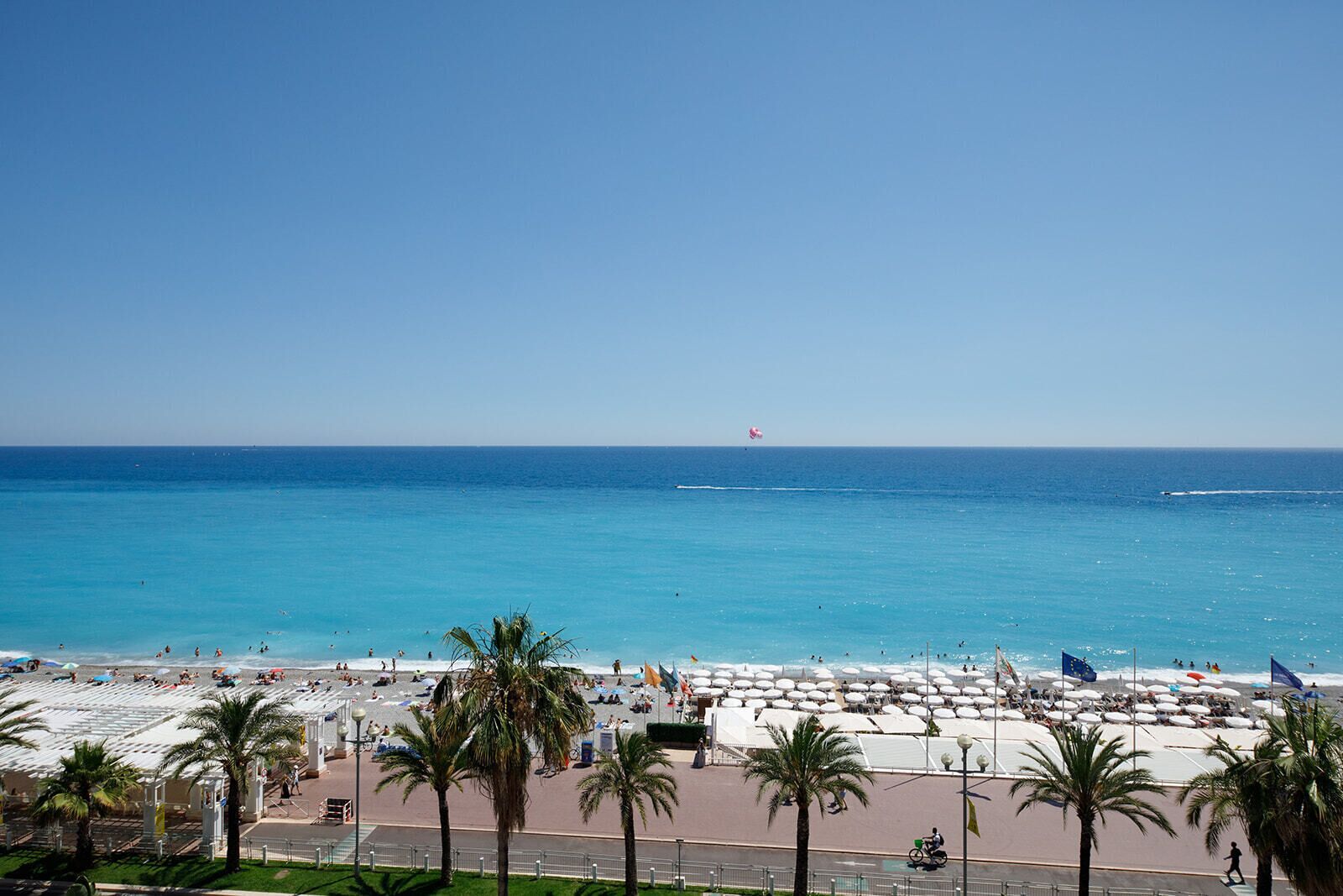 A beach with umbrellas and palm trees, a clear blue sky, and the ocean.