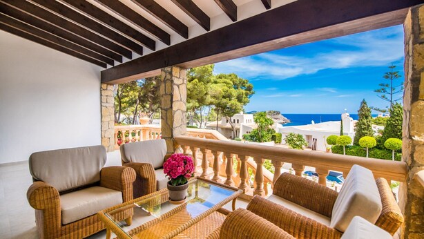 Un balcón con mobiliario de mimbre, una mesa de vidrio y vistas al mar y edificios.