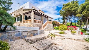 Una casa de piedra con balcón, rodeada de un jardín con diversas plantas y árboles.