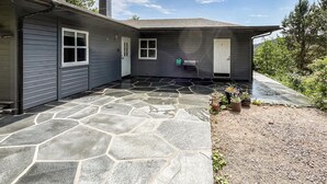 A house with a stone patio, a door, and a small garden area with potted plants.
