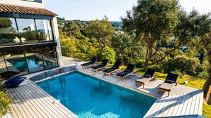 A modern outdoor swimming pool with wooden deck and lounge chairs, surrounded by trees and a view of the countryside. - Villa Croix Valmer / Gigaro, air-conditioned, beach on foot with heated swimming pool (La Croix-Valmer)