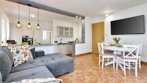 Een moderne keuken met witte kasten, een zithoek met witte stoelen, en een grijze bank met bloemenkussens.