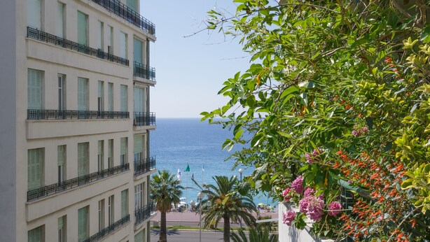 Un hotel de varios pisos con balcones, vistas al mar y abundante vegetación.