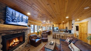 A cozy cabin interior with a stone fireplace, leather sofas, a large TV, and a kitchen area. - Timberwolf Lodge 6 2 Bedroom Cabin by RedAwning (Park City)