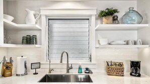 Une cuisine moderne dotée d’un évier en acier inoxydable, de meubles blancs et d’une fenêtre avec des stores horizontaux.