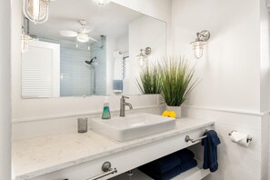 A bathroom with a white sink, a mirror, a ceiling fan, and a wall-mounted light fixture.