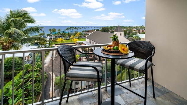 Un balcon avec deux chaises et une table, donnant sur un quartier résidentiel et offrant une vue sur l’océan.