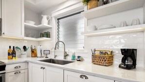 Une cuisine moderne avec des meubles blancs, un évier en acier inoxydable et une machine à café posée sur le plan de travail.