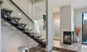 Un interior moderno con una escalera de cristal, una chimenea y una zona de comedor.