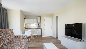 Un salon moderne avec un canapé, un téléviseur et un coin repas comprenant des chaises, et une cuisine en arrière-plan.