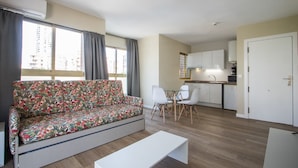 Un appartement moderne comprenant un canapé, une table à manger, des chaises, un coin cuisine et une grande fenêtre.
