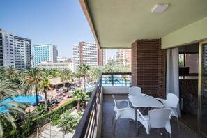 A balcony with white chairs and a table, overlooking a pool area with palm trees and a clear blue sky. - AQUARIUM II 19-3 (BENIDORM)