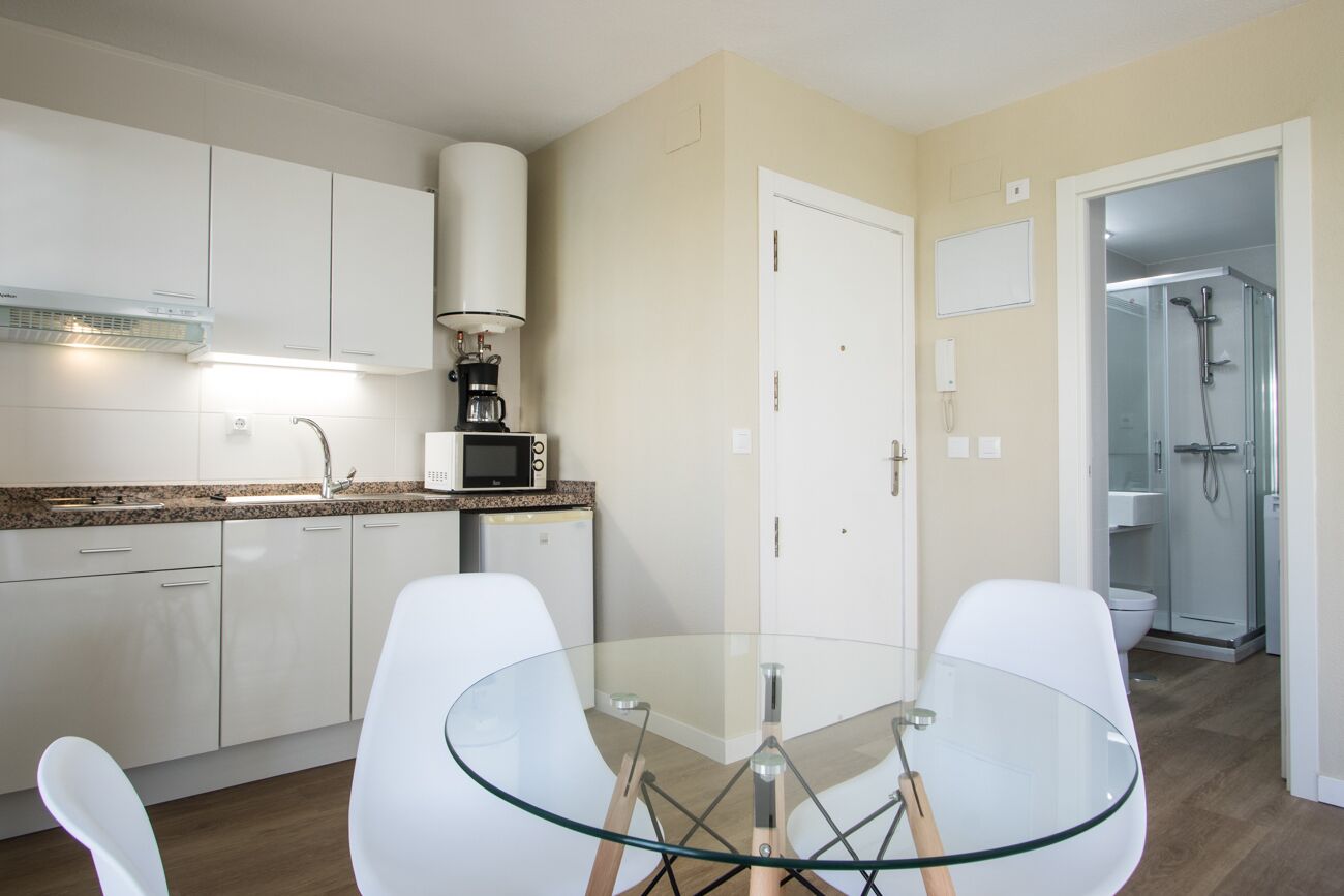 A modern kitchen with white cabinets, a glass dining table, and a coffee machine.
