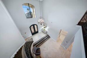 Un hall d’entrée spacieux avec un parquet en point de Hongrie, une porte noire ornée de panneaux de verre décoratifs et un lustre.