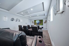 A home theater room with a flat-screen TV, reclining chairs, and a carpeted floor. - Upscale Villa with Home Theater at Reunion (Kissimmee)